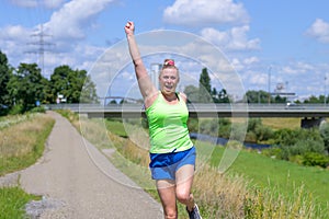 Fit healthy woman cheering as she jogs along a river bank