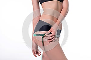 Fit and healthy young lady measuring her hips with a tape measure in centimeters and millimeters. She has her black gym