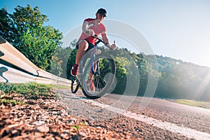 Fit male biker cyclist riding his bike cycle on an asphalt road at sunset