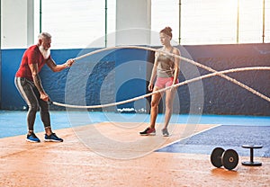 Fit man with battle rope in functional training fitness gym - Personal trainer motivating male athlete inside wellness club center