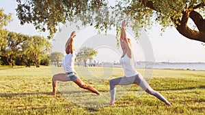 Fit man and beautiful woman practicing yoga outdoor on the grass. Sea, sky and the tree on the background. Stretching