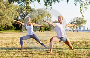 Fit man and beautiful woman practicing yoga outdoor on the grass. Stretching exercise in the sunset. Sport, fitness