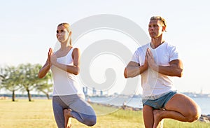 Fit man and beautiful woman practicing yoga outdoor on the grass. Stretching exercise in the sunset. Sport, fitness