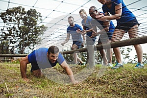 Fit man crawling under the net during obstacle course while fit people cheering