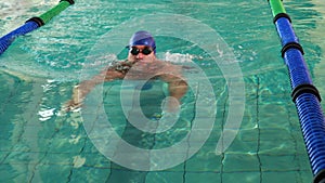 Fit man doing the breast stroke and smiling at camera in swimming pool