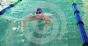 Fit man doing the breast stroke and smiling at camera in swimming pool