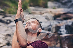 Fit man doing the eagle pose by a waterfall