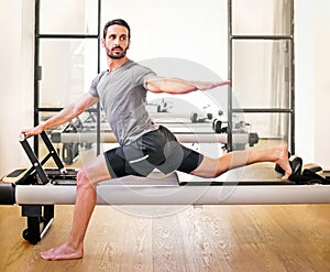 Fit man doing a lunge stretch yoga pilates exercise on reformer