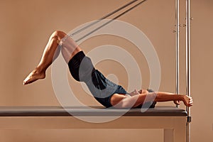 Fit man doing a lunge stretch yoga pilates exercise to strengthen and tone his muscles using a reformer in gym. Health