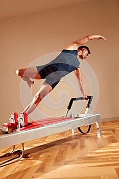 Fit man doing a lunge stretch yoga pilates exercise to strengthen and tone his muscles using a reformer in gym. Health