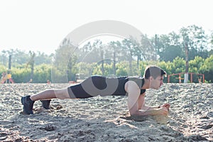 Fit man doing pank exercise during training workout on beach in summer.