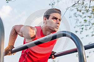 Fit man doing triceps dips on parallel bars at park exercising outdoors