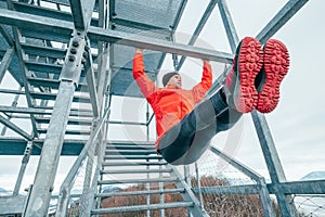 A fit man dressed in bright red sporty clothes and running shoes hanging horizontal bar training abs by raising legs. Fitness