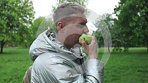 Fit man eating an apple in the countryside. Caucasian male bites an apple at spring city park. Vegan male and detox with