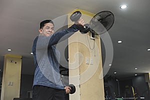 A fit man in a sweatshirt does alternating underhand front raises at an open air gym. Strict isolation shoulder workout for front