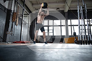 Fit man throwing medicine ball doing ball slam against gym floor or shoulder press upper body workout exercise