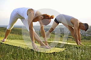 Fit man and woman in fitness clothes doing Parsvottanasana while practicing yoga together in nature in summer