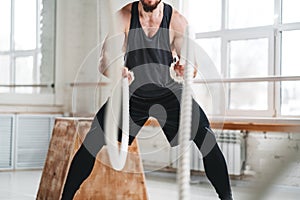 Fit man working out with battle ropes at crossfit hall