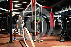Fit man working out with battle ropes at fitness gym