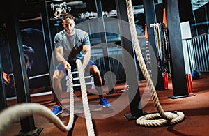 Fit man working out with battle ropes at fitness gym