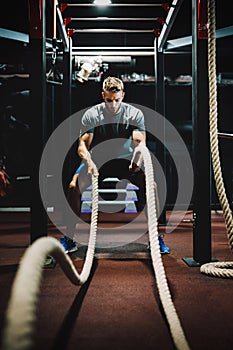 Fit man working out with battle ropes at fitness gym