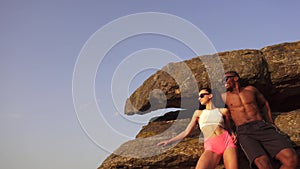 fit mixed race couple with perfect muscular bodies in sportswear posing on the rocky mountains landscape.