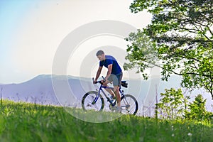 Fit mountain biker riding his bike through green grass on top of a mountain