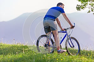 Fit mountain biker riding his bike through green grass on top of a mountain