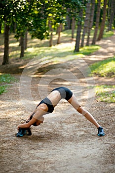 Fit, muscular girl in sportswear doing stretching exercises with her legs lateral,  on green park background