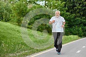 Fit old man running on racetrack in green park.