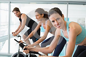 Fit people in a spin class with brunette smiling at camera