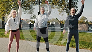 Fit people young and mature doing sports exercises outdoors on summer day