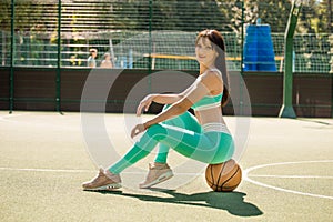 Fit pretty girl sitting on the basketball on sport playground