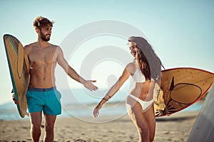 Fit, sexy, young  male and female walking and talking on beach, holding surfboards, smiling, having fun