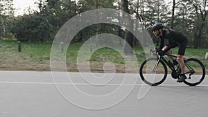Fit skinny professional cyclist riding a bicycle fast and strong pedaling out of the saddle in the park.