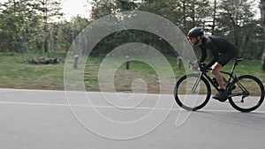 Fit skinny professional cyclist riding a bicycle fast and strong pedaling out of the saddle in the park. Slow motion