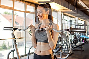 Fit slim woman lifting curl bar barbell in modern gym.