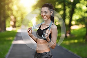 Fit smiling asian woman posing with skipping jump rope outdoors