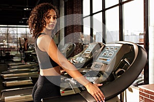 Fit smiling beautiful african american woman running on treadmill in gym