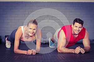 Fit smiling couple planking together in gym photo