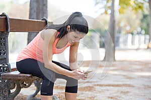 Fit sport woman looking at mobile phone internet app tracking performance after running workout sitting on park bench happy