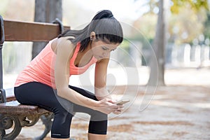 Fit sport woman looking at mobile phone internet app tracking performance after running workout sitting on park bench happy