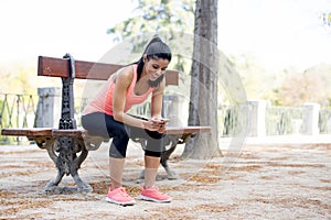 Fit sport woman looking at mobile phone internet app tracking performance after running workout sitting on park bench happy