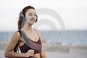 Fit sport woman relaxed listening music going to the gym. Young female athlete wearing headphone smiling on her way to