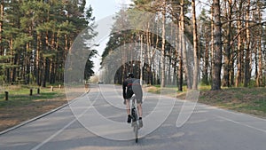 Fit sportive cyclist sprints uphill out of the saddle. Training on road bicycle. Back side follow shot. Slow motion