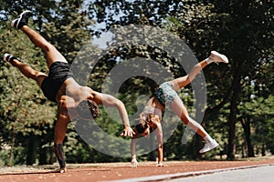 Fit sports couple of athletes practicing cartwheels in sunny park. Outdoor training in natural environment inspires with