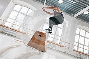 Fit sportsman doing jump exercises on wooden box in cross workout gym