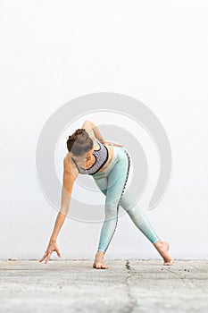 Fit sporty active girl in fashion sportswear doing yoga fitness exercise in front of gray wall, outdoor sports, urban