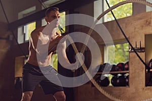 Fit, sporty and athletic sportsman working in a gym. Man training using battle ropes. Cross fit, sports, athletics and