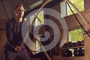 Fit, sporty and athletic sportsman working in a gym. Man training using battle ropes. Cross fit, sports, athletics and